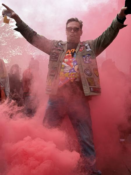A man celebrates in a crowd surrounded by red smoke